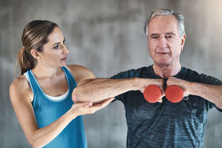 Getting older and getting healthier. a senior man using weights with the help of a physical therapist.の写真素材