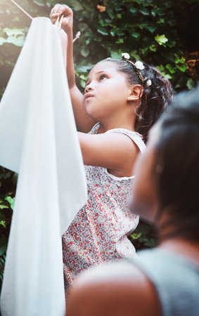Teach kids responsibility by getting them involved in chores. a mother and her little daughter hanging up laundry on a washing line outdoors.の写真素材