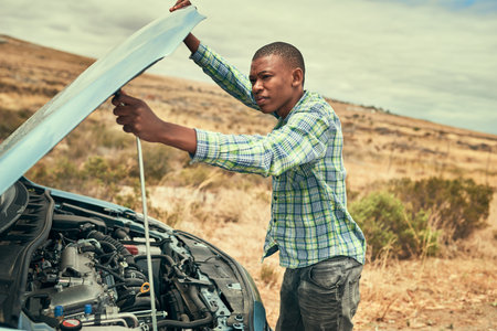 Pop the hood. a young man checking under the hood of his car after breaking down.