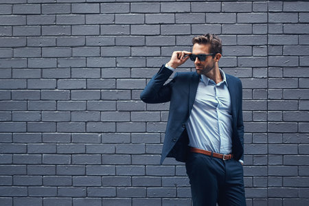 Success never goes out of style. a handsome young businessman standing against a grey facebrick wall.の写真素材