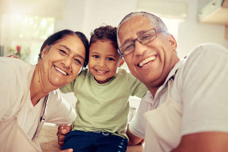 Grandparents, grandkid and family smile, happy and playing together at home. Portrait face of love, bond and relaxing elderly grandma, grandpa and young kid for funny, care and childhood developmentの写真素材