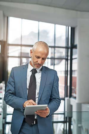 Taking a closer look at some data. a mature businessman working on a digital tablet in a modern...