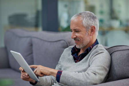 Catching up with the morning financials. a mature businessman using a digital tablet while sitting...