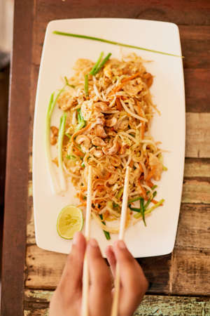 Pad thai anyone. a person eating a bowl of pad thai in a restaurant in Thailand.の写真素材