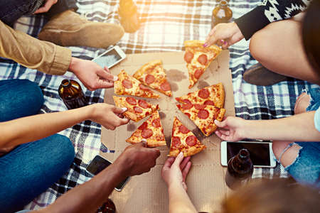 Gather around for a slice of the best. a group of friends eating pizza while having a picnic.の写真素材