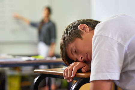 This class is a snoozefest. a young schoolboy sleeping on his desk in class.の写真素材