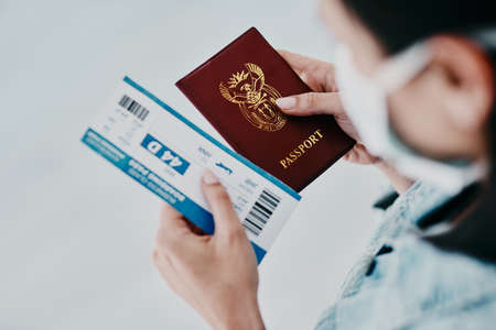 Travel, covid and tourist visa or passport while holding a plane flight ticket with face mask at airport for immigration. Closeup of female traveler holding ID for traveling during corona pandemicの写真素材