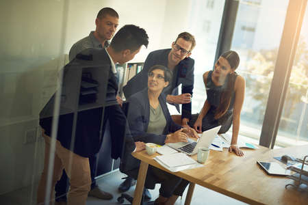 Execution is the key to a successful business. a group of coworkers discussing something on a laptop during a meeting.の写真素材