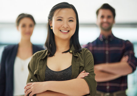 Its easy to be confident with a great team behind you. Portrait of an attractive young businesswoman standing with her arms crossed with two colleagues in the background.の写真素材