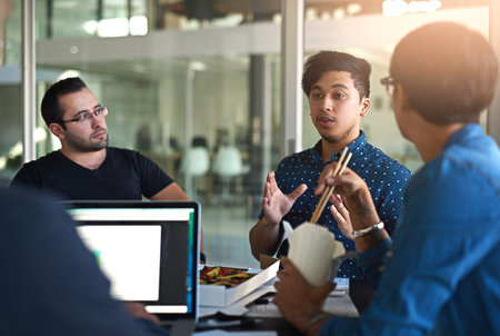 Putting his idea forward. a group of colleagues eating while having a meeting in the boardroom.の写真素材