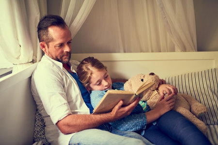 Once upon a time...a father reading a story to his little daughter at home.の写真素材