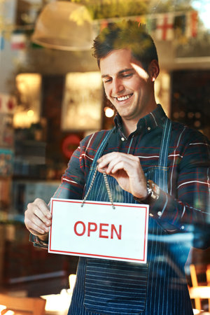 Im open for business. Closeup shot of a young man hanging up an open sign in a shop window.