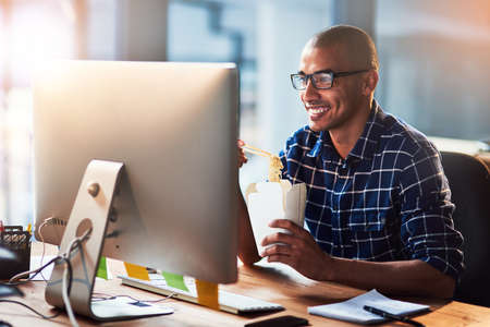 Hes always hungry for success. Portrait of a young designer eating takeaways while working at his...