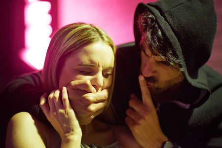 Be quiet and do as I say. a frightened young woman being grabbed by a criminal in the city.