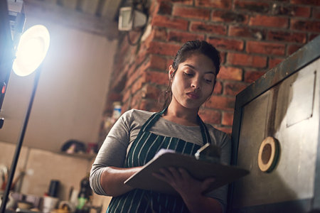 She makes a note of every detail in her business. a young entrepreneur writing on a clipboard in a workshop.の写真素材