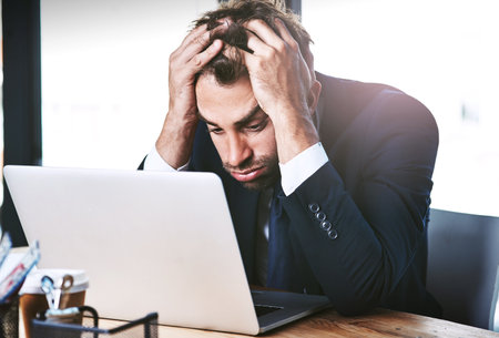 He just cant figure it out. a handsome young businessman looking stressed while working on his laptop in the office.の写真素材