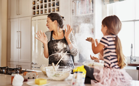 Getting messy is part of the fun of baking together. two little girls having fun while baking with their mother in the kitchen.の写真素材