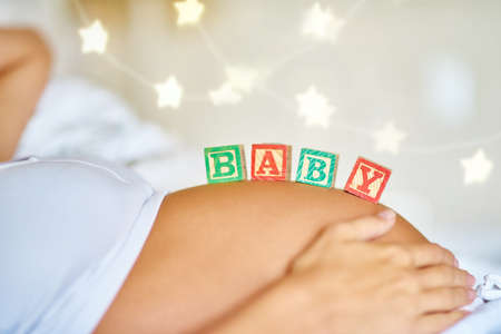 Baby on board. Closeup shot of a pregnant woman lying down with wooden baby blocks on her belly.の写真素材