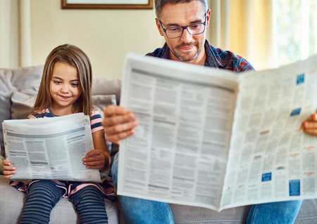 Reading the news, just like her dad. a handsome mature man and his daughter reading the morning paper.の写真素材