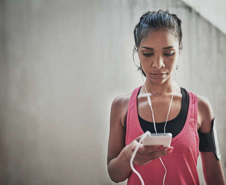 Selecting her favourite workout tracks. a sporty young woman listening to music while exercising outdoors.の写真素材