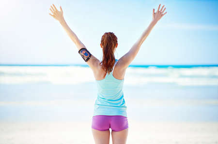 Rearview shot of a young woman standing with her arms outstretched on the beach.