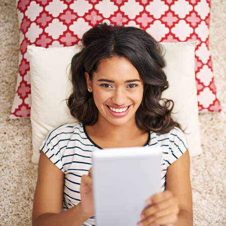 My social feeds are buzzing. High angle portrait of a young woman using her tablet while relaxing at...