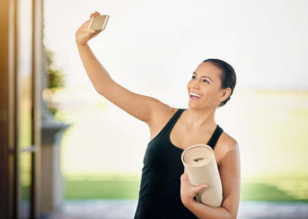 Yoga selfie. a young woman taking a selfie while carrying her yoga mat.
