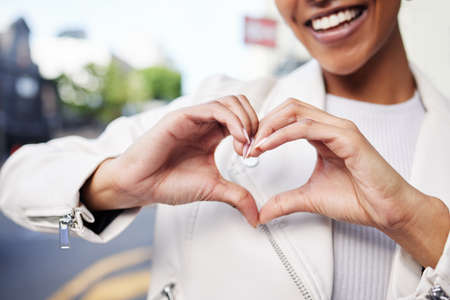 Hands, heart and sign of a black woman with smile in care, support and joy against city background. Happy African American female happy and smiling with love gesture or hand sign at a urban townの写真素材