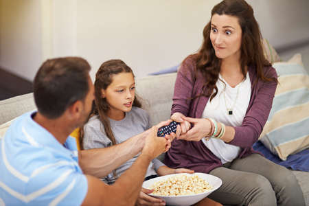 I think its the girls turn tonight. a young family watching a movie from the sofa.
