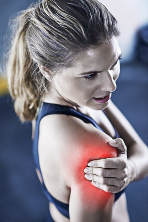 Sore is the most satisfying pain. a young woman holding her injured shoulder thats highlighted in...