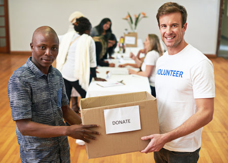 We accept any and all donations. Cropped portrait of two volunteers carrying a donations box.