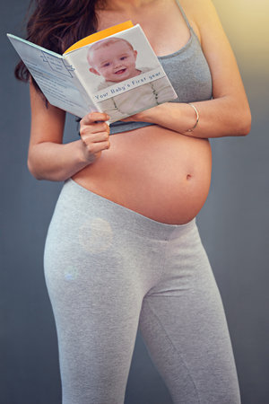 Dont panic, theres a book for that. a pregnant woman reading a babybook against a gray background.