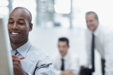 They are going to love this. Handsome African businessman writting on flipchart and smiling with colleagues watching in the background.の写真素材