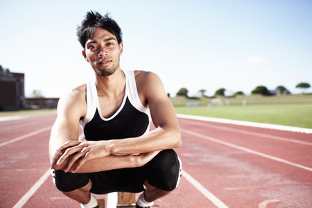 He is highly focussed and determined to win. A young runner crouching on a race track.の写真素材