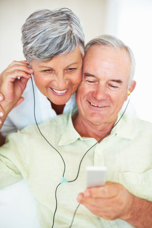Mature couple listening music at home. Handsome mature man and woman listening music at home.の写真素材