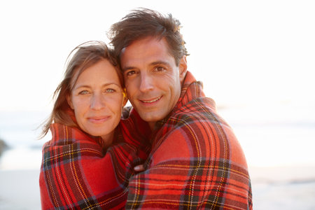 Wrapped up in each other. A devoted and affectionate couple wrapped in a blanket on the beach.