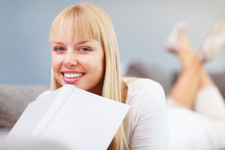 Beautiful woman with a book at home. Closeup of beautiful young student lying down with a book.の写真素材