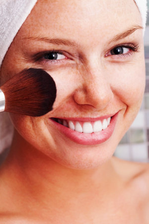 Closeup of a happy woman applying make up to face after a bath. Closeup of a smiling young female applying make up to face after a bath.の写真素材