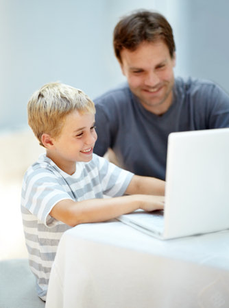 Showing dad a thing or two. Young boy on his laptop with his father next to him.