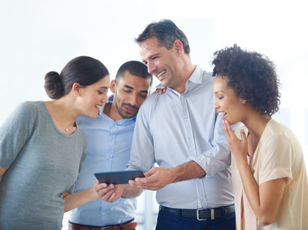 Sharing online jokes. a group of colleagues using a digital tablet together in an office.