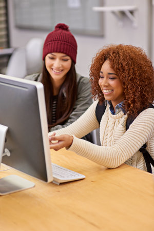 Using online resources to their advantage. two female students studying together at a computer in the library.の写真素材