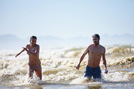 Sharing a summer getaway. a laughing young couple walking out of the surf together.の写真素材