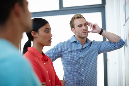 Theyve got their thinking caps on. a group of young designers brainstorming at a whiteboard.