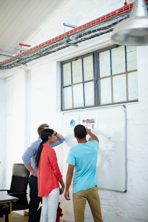 Working together towards their vision. a group of young designers brainstorming at a whiteboard.