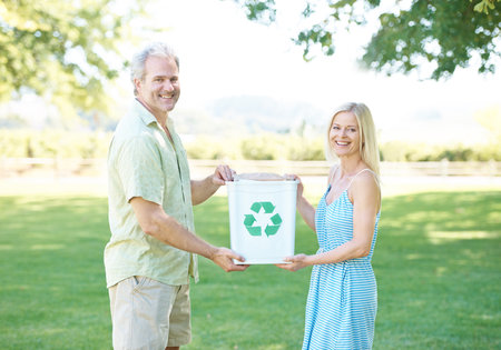 We hold the future in our hands. A happy couple standing in a park holding a recycling bin and...