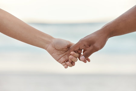 Touch, love and support with interracial couple holding hands in a committed, loving and close relationship. Closeup hands of man and woman enjoying beach travel, sea vacation or holiday and romanceの写真素材