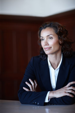 Considering the days events. Mature female advocate looking away from the camera while sitting with her arms folded and smiling slightly.の写真素材