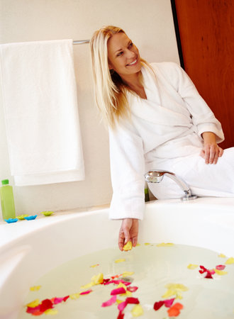 Make your home into a spa. A beautiful young woman sitting on the edge of a luxurious bath filled with petals.の写真素材