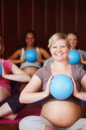Staying in shape boosts the babys health too. A group of pregnant women exercising their arms in a yoga class using exercise balls.の写真素材