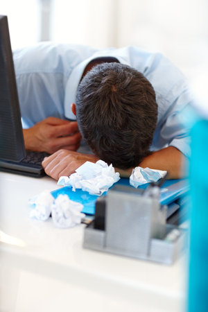 I shouldve made a pillow with all these balls of paper. a businessman in despair with his head on his desk.の写真素材